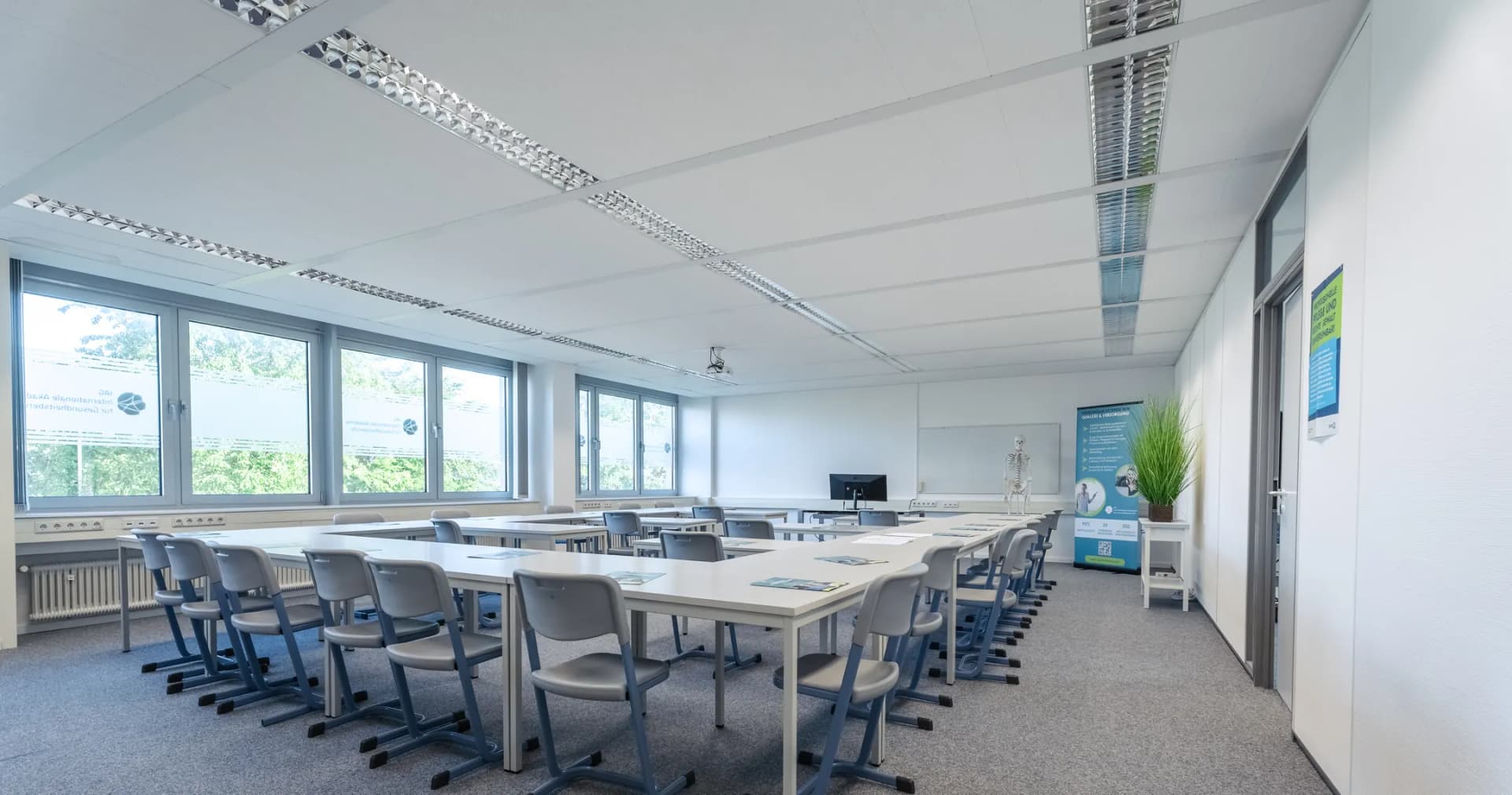 Kursraum mit Tischen in U-Form, Bildschirm, Whiteboard und Skelettmodell